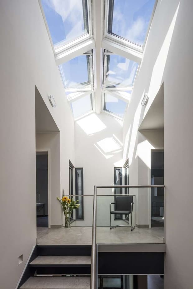 Heller Flur mit Glasdach, Oberlichtern, moderner Treppe, Glasgeländer, weißen Wänden und stilvollem minimalistischen Design.