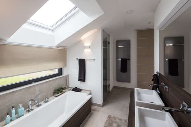 Modernes Badezimmer mit Badewanne, Doppelwaschbecken, Glasdusche, Dachfenster, Handtüchern und stilvoller Beleuchtung.