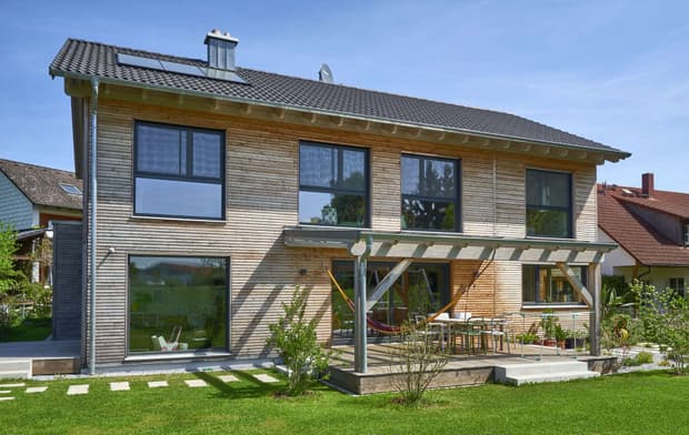 Die Terrasse des modernen Holzhauses im Landhausstil mit Holzfassade aus Lärchenholzbohlen und Doppelcarport