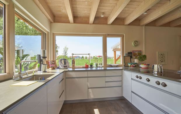 Die Küche des modernen Holzhauses im Landhausstil mit Holzfassade aus Lärchenholzbohlen und Doppelcarport