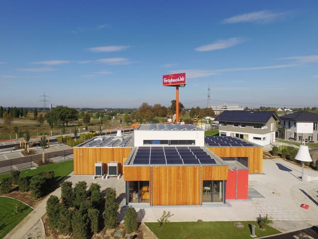 Modernes Gebäude mit Holzfassade und Solarpanels auf dem Dach im Musterhauspark bei sonnigem Wetter.