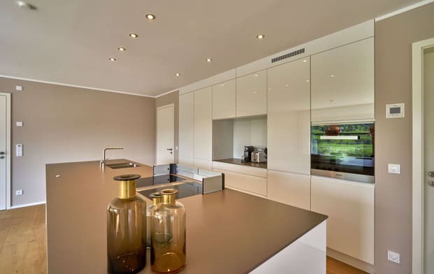 Die Küche des modernen Holzhauses mit drei Gebäudetrakten, davon zwei mit mineralischem Außenputz und einer mit Holzverschindelung, alle mit Flachdach und im Bauhausstil