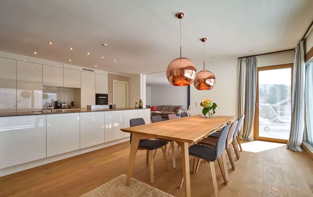 Das Esszimmer des modernen Holzhauses mit drei Gebäudetrakten, davon zwei mit mineralischem Außenputz und einer mit Holzverschindelung, alle mit Flachdach und im Bauhausstil