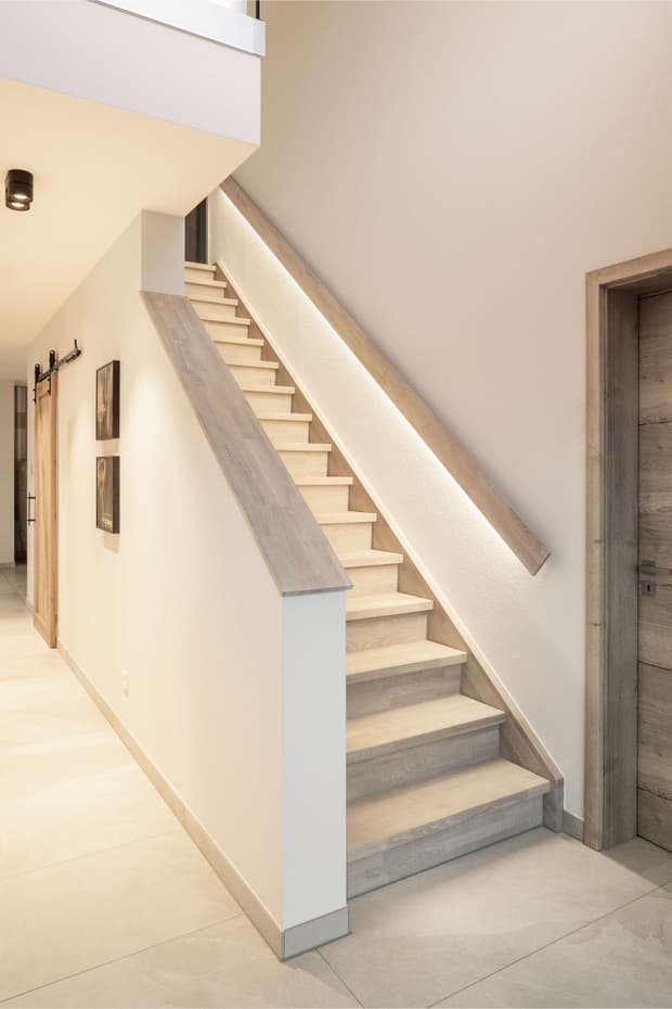 Moderner Hausflur mit heller Holztreppe, LED-Handlauf, beigem Fliesenboden und minimalistischer Wandgestaltung