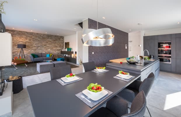 Offene moderne Küche mit Esstisch, Designleuchte, grauen Möbeln, Steinwand, Wohnbereich und stilvoller Dekoration.
