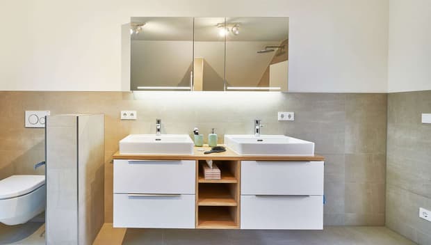 Modernes Badezimmer mit Doppelwaschbecken, großem Spiegel, hellen Fliesen, Holzdetails und integrierter Beleuchtung.