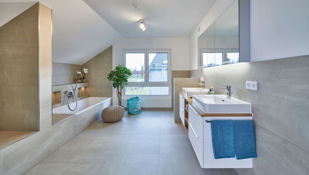 Modernes Badezimmer mit Badewanne, Doppelwaschbecken, großen Fliesen, Dachschräge, Fensterfront und blauen Handtüchern.