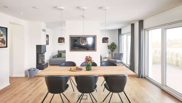 Helles Esszimmer mit Holztisch, schwarzen Stühlen, Kamin, großen Fenstern, Parkettboden und moderner Dekoration.