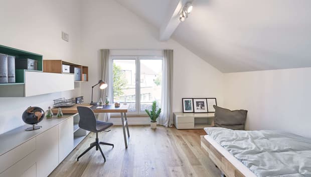 Helles Jugendzimmer mit Schreibtisch, Bett, Holzfußboden, Dachschräge, großen Fenstern und moderner Einrichtung.