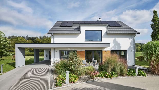 Modernes Einfamilienhaus mit Satteldach, Solarpanelen, Carport, großer Fensterfront, Garten und Terrasse im Grünen.
