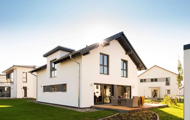 Modernes Einfamilienhaus mit Satteldach, weißer Fassade, Terrasse, großen Fenstern und gepflegtem Garten bei Sonnenschein.