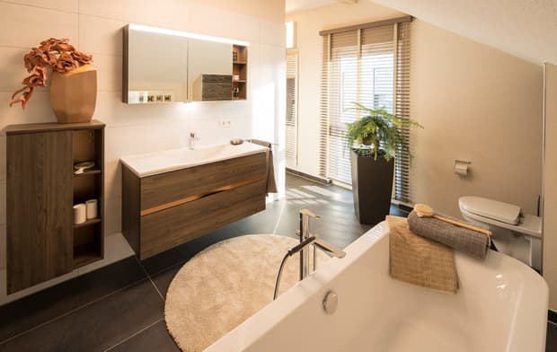 Modernes Badezimmer mit freistehender Badewanne, Holzwaschtisch, Spiegel, Pflanzen, WC und warmer Beleuchtung.