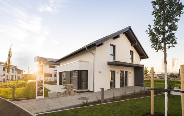 Modernes Einfamilienhaus mit Satteldach, weißer Fassade, großen Fenstern, Terrasse und gepflegtem Garten bei Sonnenuntergang.
