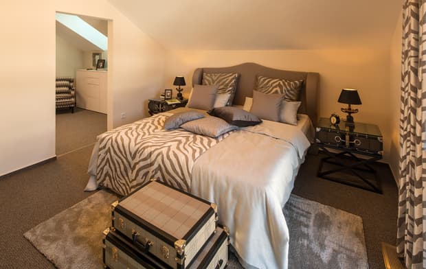 Modernes Schlafzimmer mit Doppelbett, Zebra-Bettwäsche, Nachttischen, Lampen, Teppich und Koffern als Dekoration.