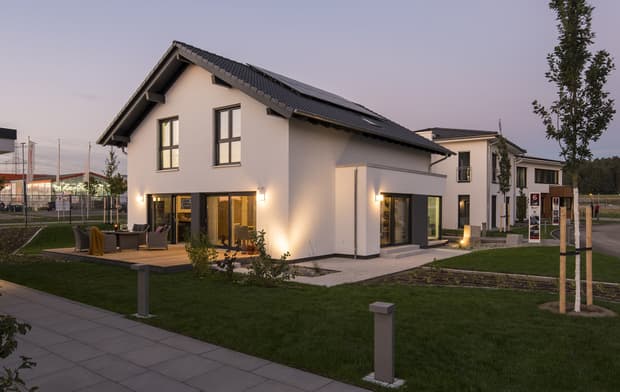 Modernes Einfamilienhaus mit Satteldach, Solarpanelen, Terrasse, großen Fenstern und Garten bei Abendbeleuchtung.