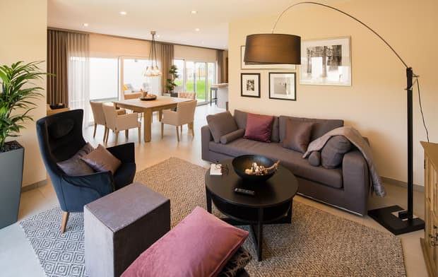 Modernes Wohnzimmer mit grauem Sofa, Sessel, Esstisch, Teppich, Stehlampe, Wandbildern und gemütlicher Beleuchtung.