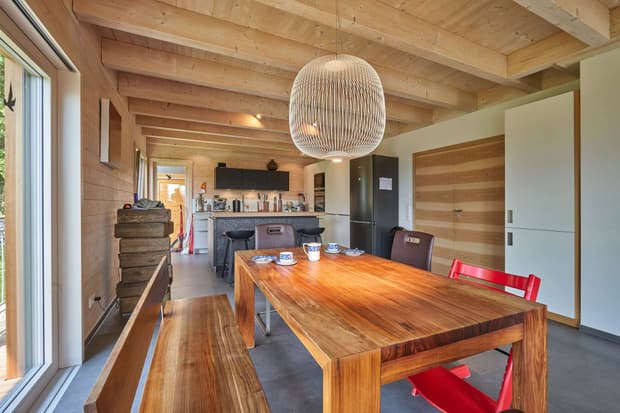 Das Esszimmer des modernen Holzhauses im Landhausstil mit Holzfassade, Holz-Alu-Fenstern und großzügigen Balkonen