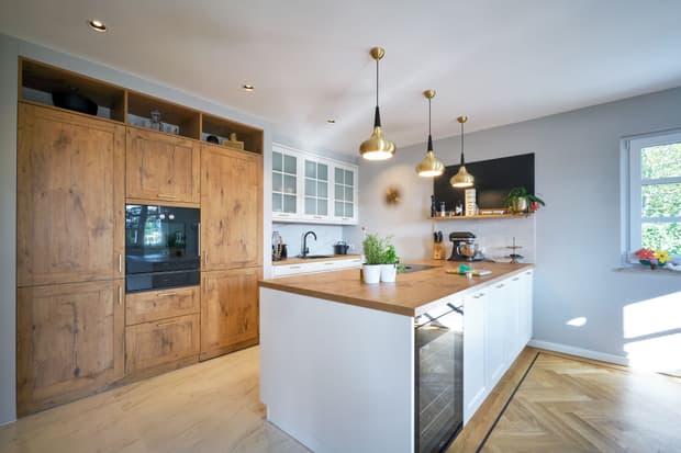 Die moderne Küche des modernen, mediterranen Holzhauses im Stil einer Stadtvilla mit weißem, mineralischem Außenputz und grünen Fensterläden