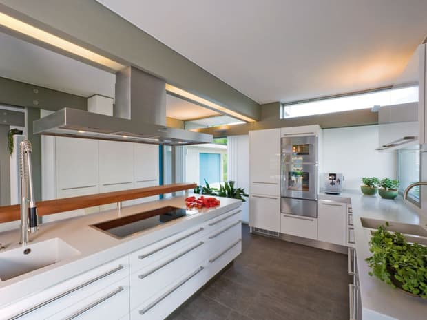 Moderne Designerküche mit Kochinsel, weißen Fronten, Sichtbalken, indirekter Beleuchtung und hochwertigen Geräten