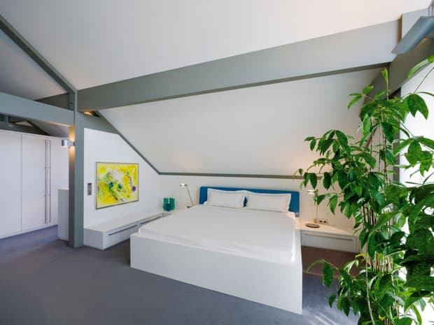 Modernes Schlafzimmer mit Dachschräge, Sichtbalken, Doppelbett, Einbauschrank, Grünpflanze und minimalistischem Design