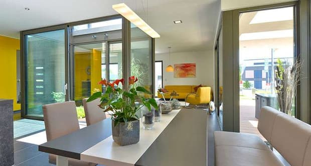 Moderner Essbereich mit grauem Tisch, beigen Stühlen, roten Blumen und Blick in Wohnzimmer mit gelber Couch