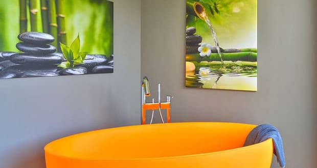 Orangefarbene freistehende Badewanne aus Kunststoff mit Handtuch in modernem Badezimmer mit grüner Wanddekoration