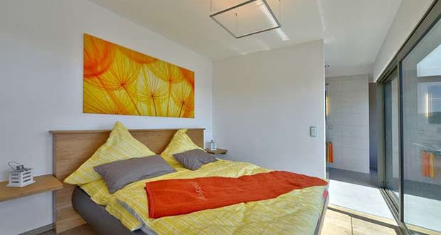 Modernes Schlafzimmer mit gelber Bettwäsche, orangener Decke und großem Fenster mit Sonnenlicht