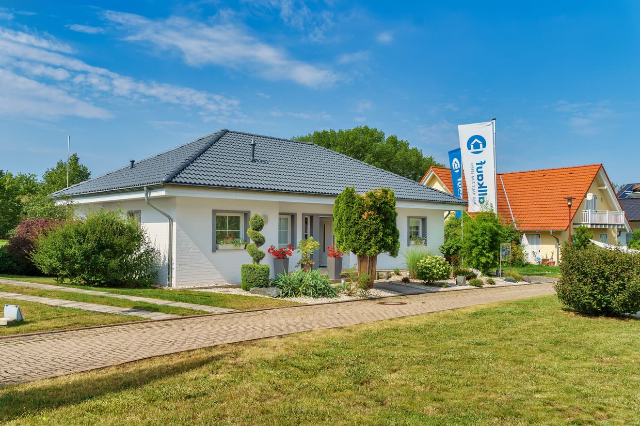 Modernes weißes Einfamilienhaus mit grauem Ziegeldach und gepflegtem Garten an sonnigem Tag