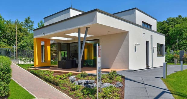 Modernes weißes Kubushaus mit gelbem Stützpfeiler große Glasfront und Garten im Sonnenschein
