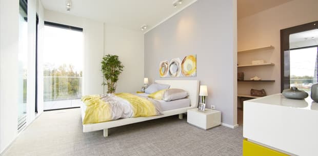 Modernes helles Schlafzimmer mit großem Fenster, weißem Bett, gelb-grauer Bettwäsche und Pflanzenbeleuchtung