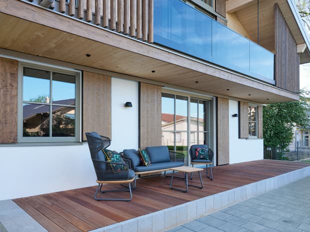 Die durch den Balkon überdachte Terrasse des modernen und großzügigen Holzhauses, bzw. Massivholzhauses im Landhausstil im Musterhauspark in Ortenburg. Der Neubau erinnert an die Chalets im Alpenvorland, hat aber viele moderne Designelemente.