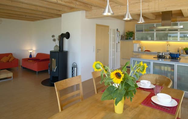 Der Wohn- und Essbereich des modernen Holzhauses mit ergrauter Lärchenholzfassade, ohne Dachüberstand für schnelle und gleichmäßige Ergrauung mit Kachelofen