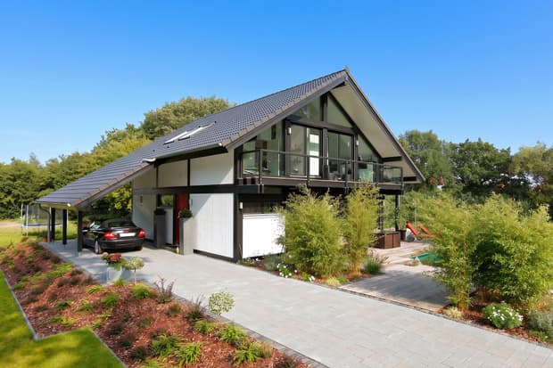 Modernes Haus mit schwarzem Pultdach, weißer Fassade, großem Balkon und gepflegtem Garten bei Sonnenschein