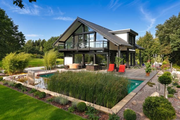 Modernes zweistöckiges Haus mit großem Garten, Holzzierde, Teich und Pool, umgeben von grünen Bäumen unter blauem Himmel