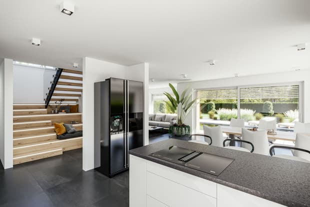 Moderne offene Küche mit schwarzem Kühlschrank, Kochinsel, weißen Möbeln und Treppe mit integrierter Beleuchtung in hellem Wohnraum