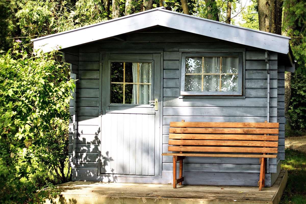 Graues Gartenhaus aus Holz mit brauner Holzbank davor