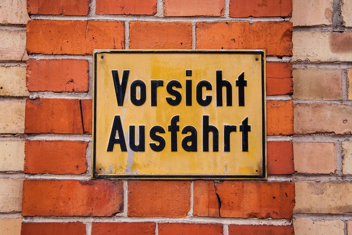 Gelbes Schild an einer Wand mit Aufschrift "Vorsicht Ausfahrt"