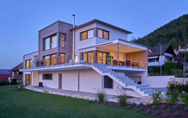 Modernes Holzhaus mit drei Gebäudetrakten, davon zwei mit mineralischem Außenputz und einer mit Holzverschindelung, alle mit Flachdach und im Bauhausstil