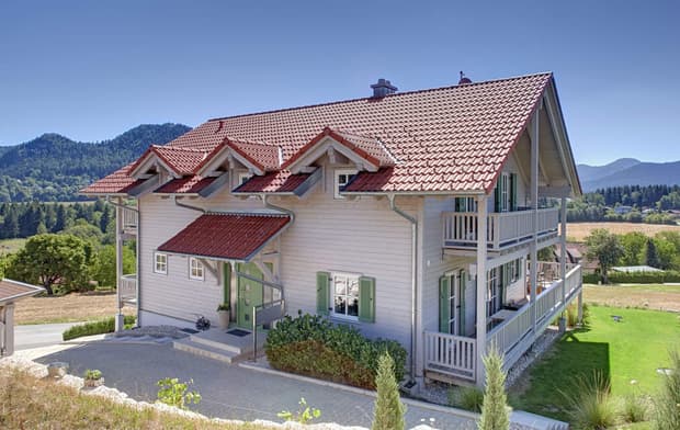 Der Eingang des Holzhauses im Landhausstil mit Holzfassade und mehreren Balkonen, drei Giebeln und vielen Fenstern