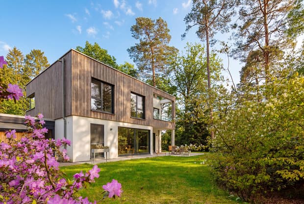 Modernes zweistöckiges Haus mit Holzfassade und großem Garten umgeben von bunten Blumen und hohen Bäumen