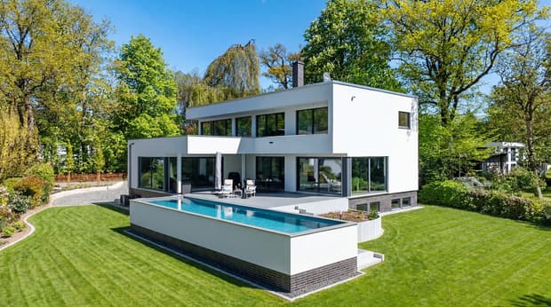 Modernes zweistöckiges weißes Haus mit großen Fenstern, Terrasse und langem rechteckigem Pool umgeben von grünem Garten