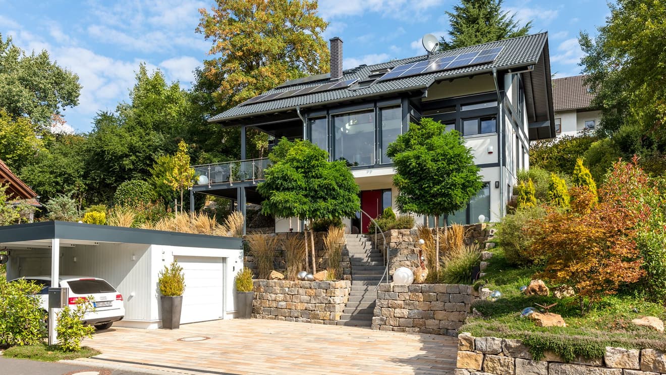 Außenansicht des modernen Fachwerkhauses in Hanglage mit Garage und Carport