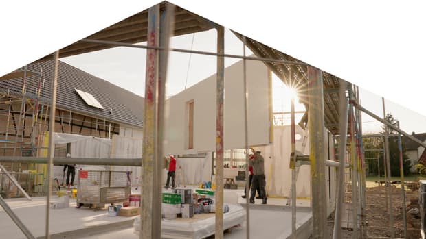 Baustelle mit weißen vorgefertigten Wandpaneelen und Bauarbeitern in Schutzhelmen bei Hausbau im Freien