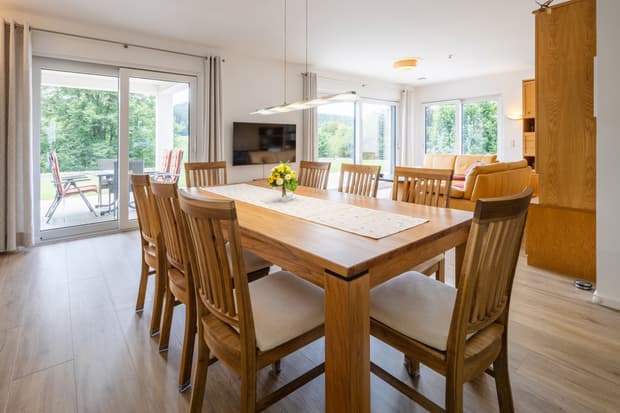 Esszimmer mit großem Holztisch und sechs Stühlen, bodentiefe Fenster mit Blick auf Terrasse und Garten