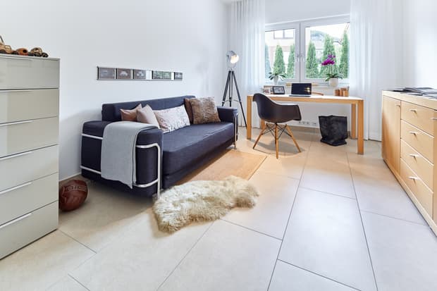 Helles modernes Arbeitszimmer mit blauem Sofa, Holztisch, schwarzem Stuhl und weißen Fliesenboden