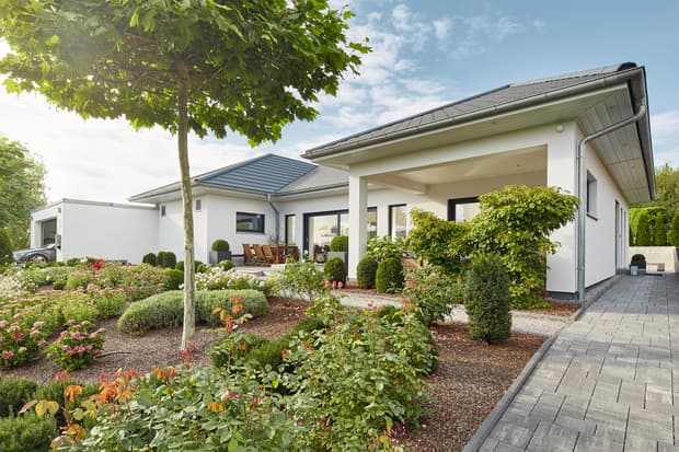 Moderner weißer Bungalow mit schwarzem Dach, gepflastertem Weg und gepflegtem Garten mit Blumen und Sträuchern