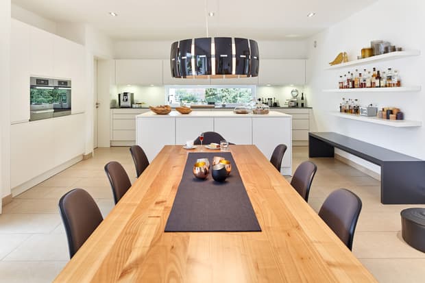 Moderner Essbereich mit Holztisch und schwarzen Stühlen vor weißer Küche mit Kücheninsel und Deckenlampe