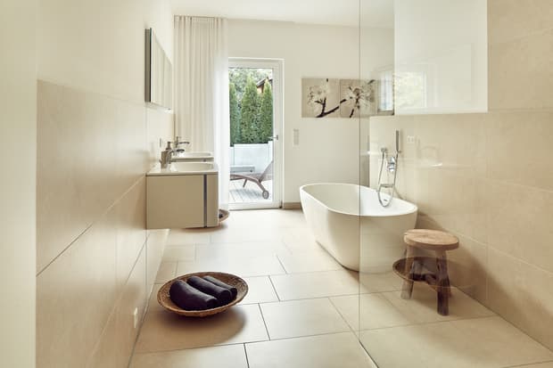 Modernes Badezimmer mit freistehender Badewanne, zwei Waschbecken, beige Fliesen und Zugang zu Terrasse mit Gartenmöbeln