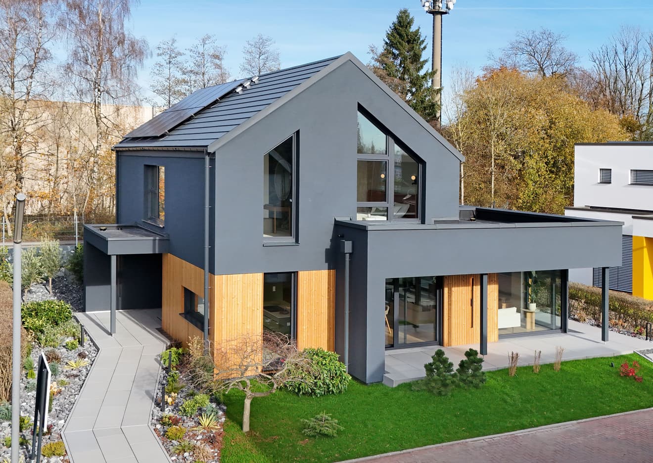 Modernes Einfamilienhaus mit grauer Fassade und Holzverkleidung umgeben von Garten und Herbstbäumen