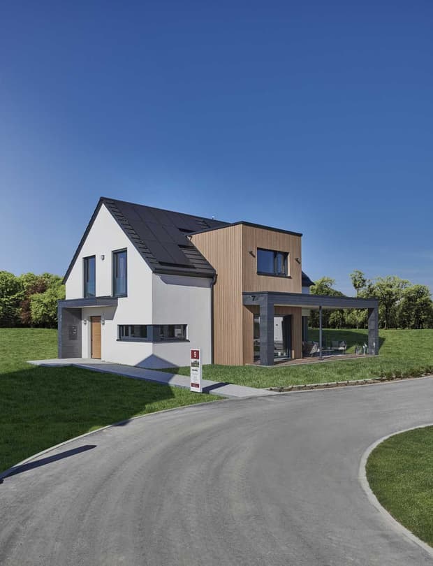 Modernes Musterhaus mit Satteldach, Holzfassade, großer Terrasse und Panoramafenstern in grüner Umgebung.
